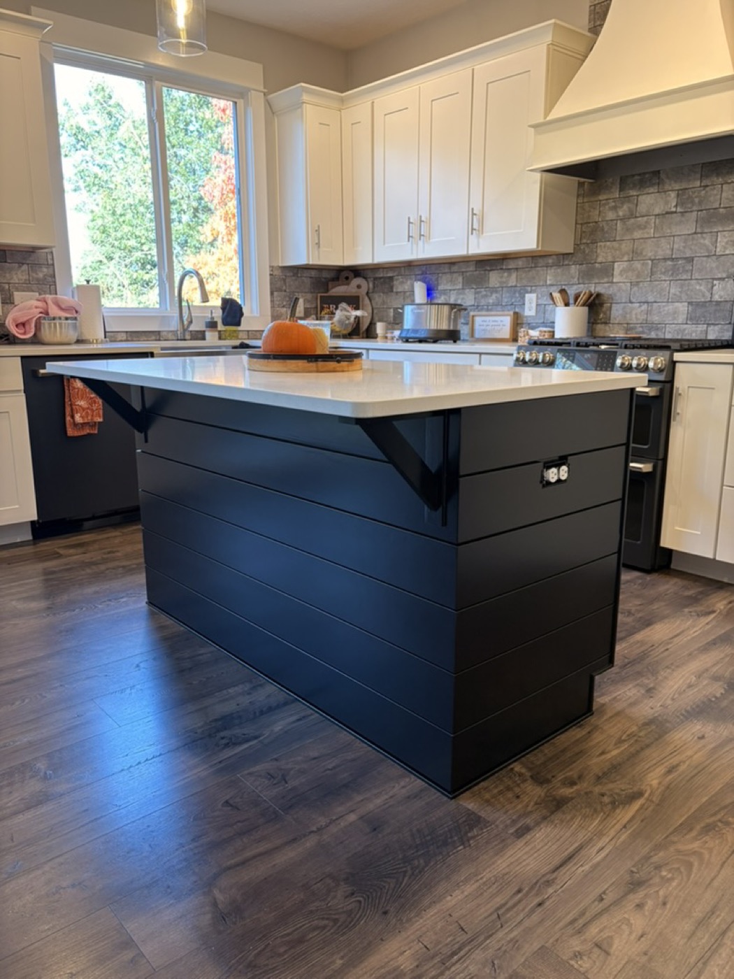 Kitchen with a painted black island, white cabinetry and stone backsplash