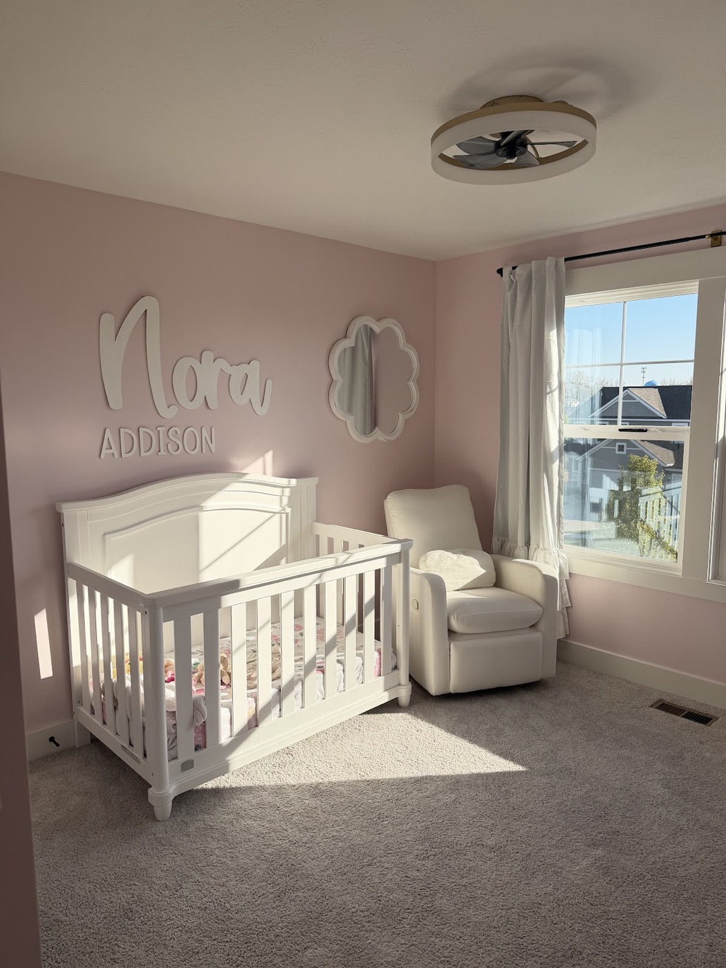 Pink nursery with a wall-mounted name decal above a white crib