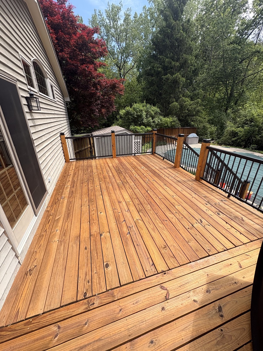Stained wood deck with black railings next to a covered pool