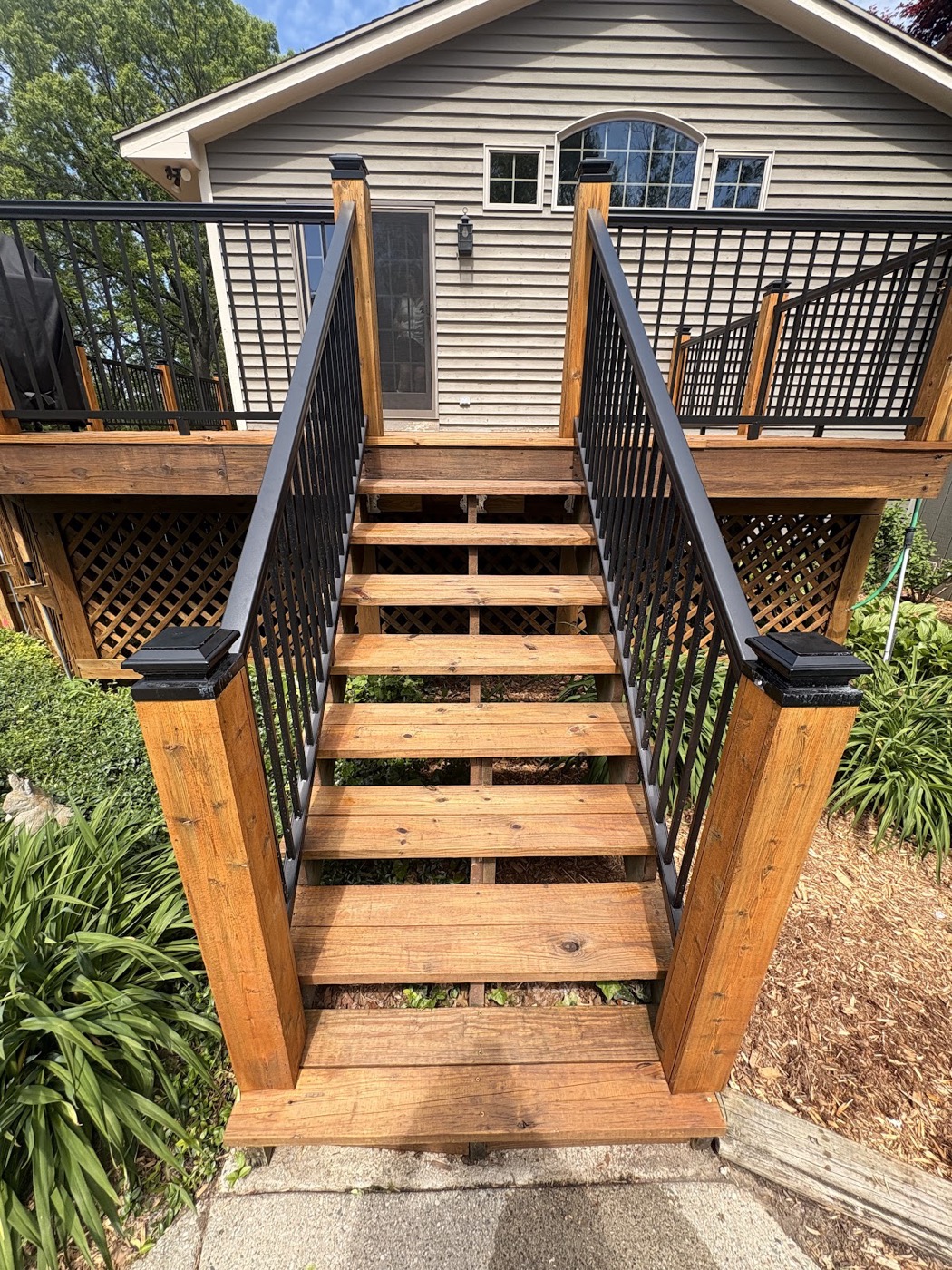 Stained wood deck staircase with black metal railings leading up to a house
