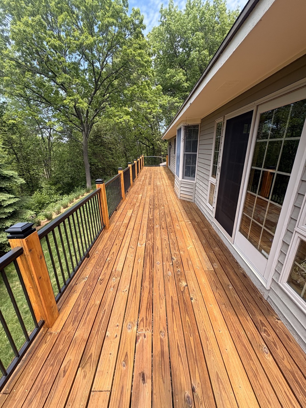 Long stained wood deck walkway along the side of a house with black metal railings
